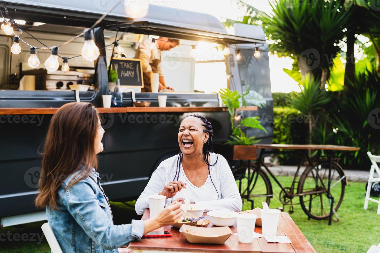 Happy multiracial senior friends having fun eating in a street food truck market photo