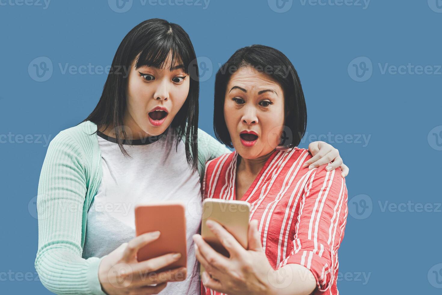 Asian mother and daughter using mobile smartphones outdoor - Happy Chinese family having fun with new trends technology apps for social media - Concept of social people addiction with parenthood photo