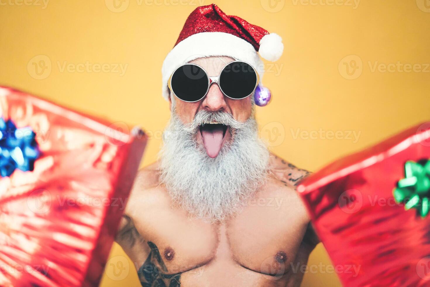 Tattooed fit santa claus doing crazy and giving christmas gifts - Trendy beard hipster senior wearing xmas clothes and holding presents - x-mas Celebration and holidays concept photo