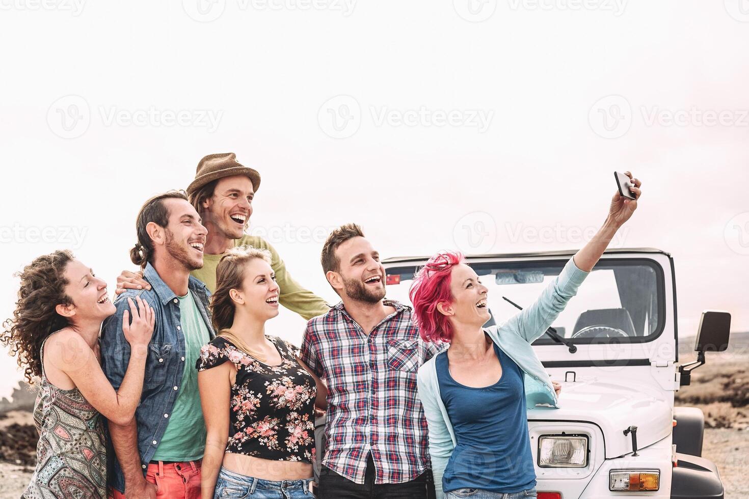 Happy friends taking selfie with mobile smartphone next offroad convertible car - Millennial young people having fun making road trip - Vacation, tech and youth holidays lifestyle concept photo