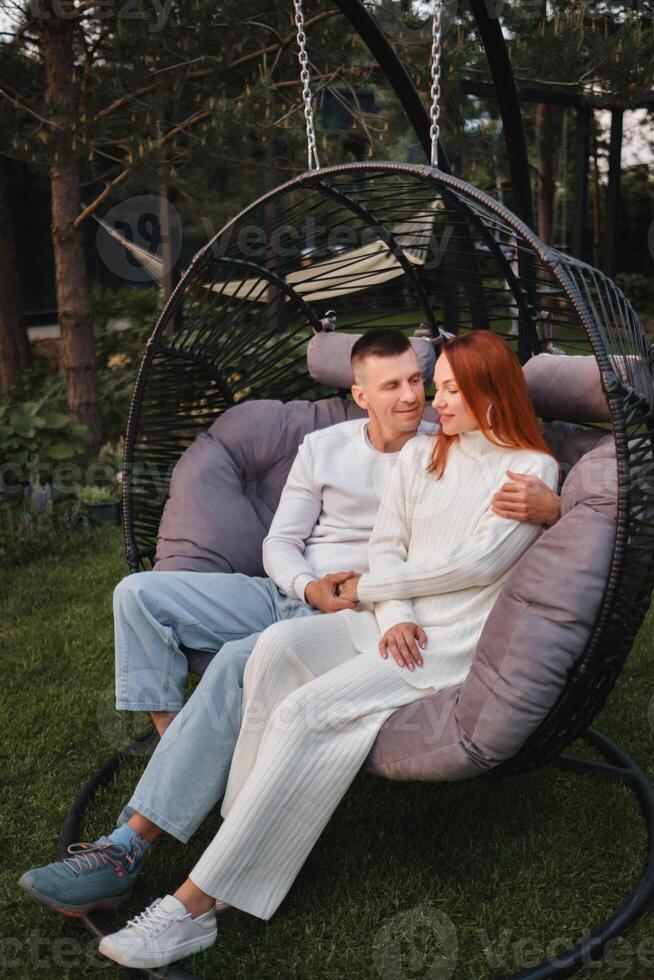 A happy family is sitting in a hammock on the lawn near the house photo