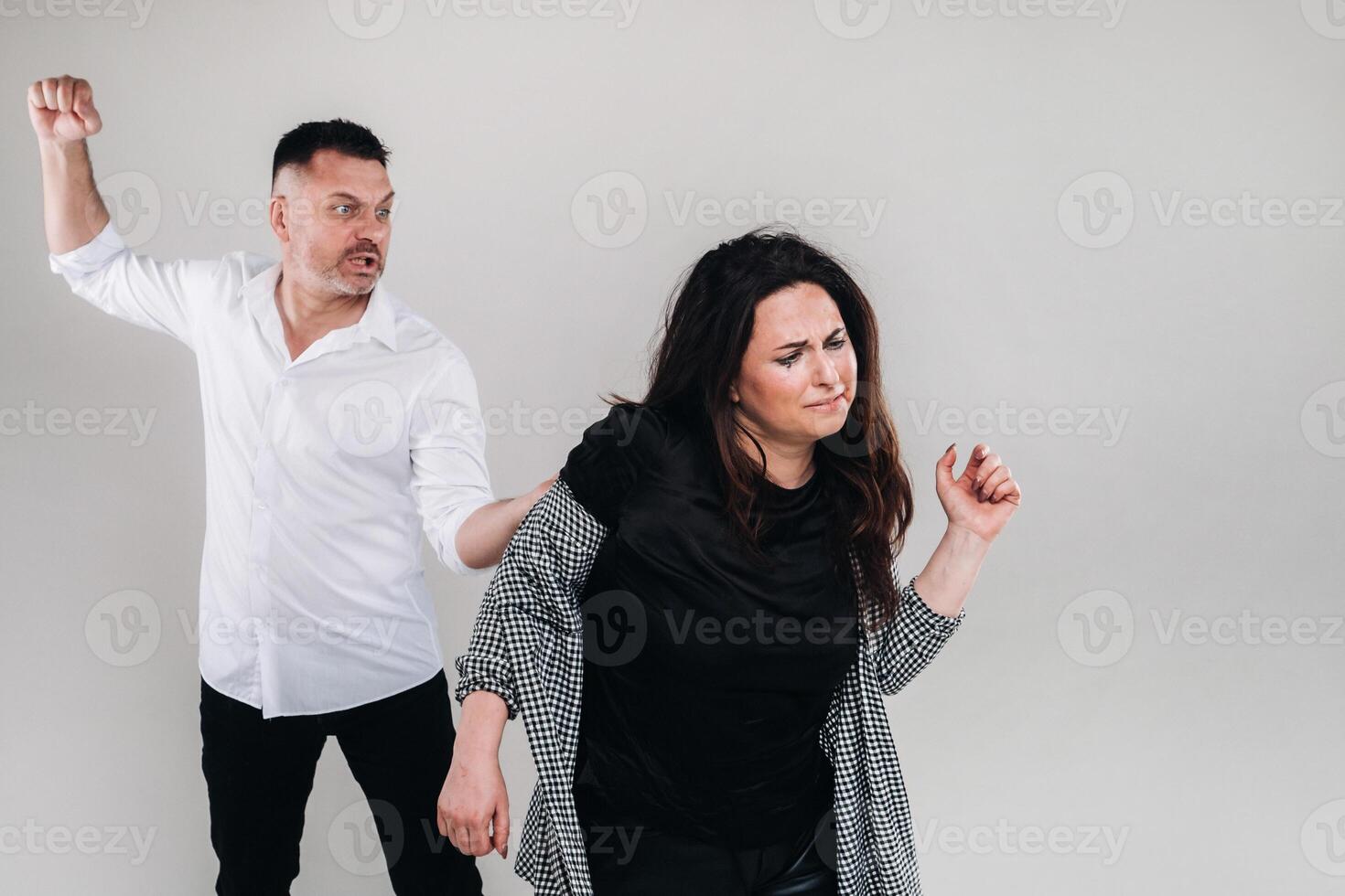 A man swings his hand at a battered woman standing on a gray background. Domestic violence photo