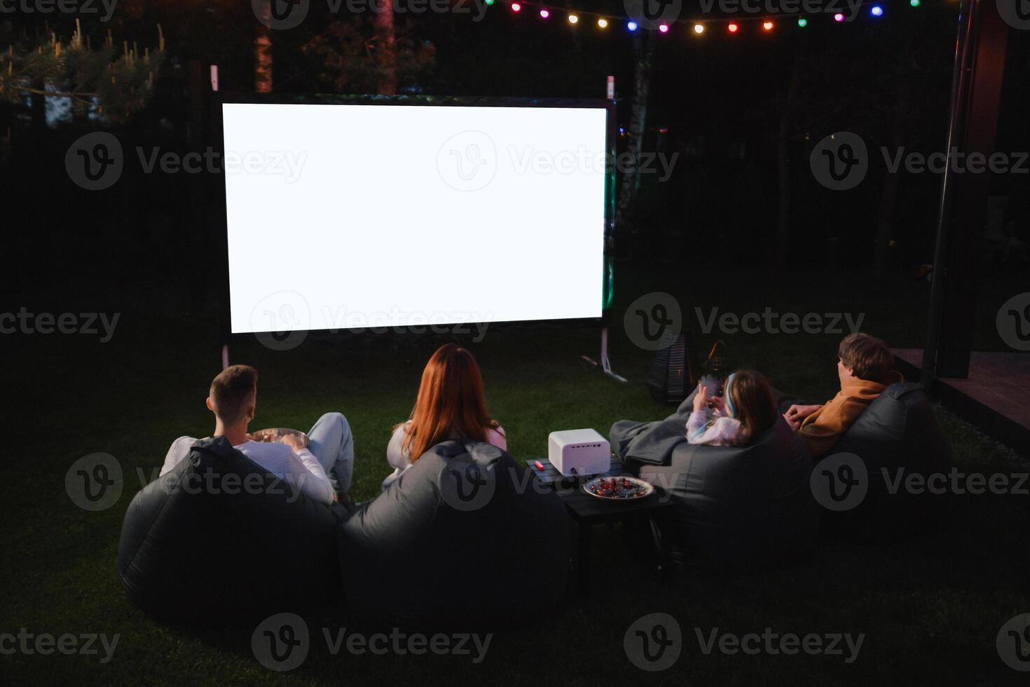 family mother, father and children watch a projector, movies with popcorn in the evening in the courtyard photo