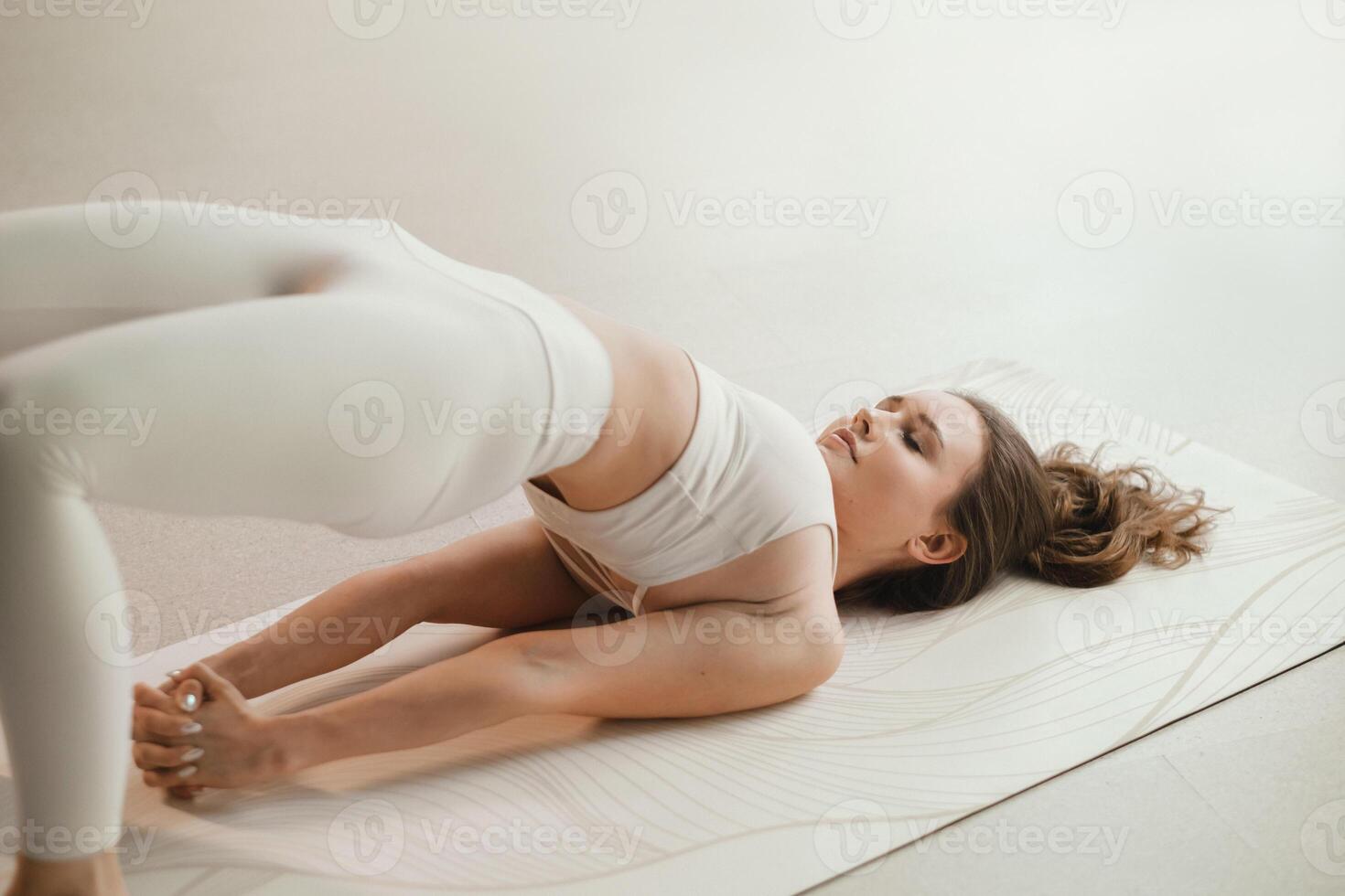 A girl in white clothes does yoga lying on a rug indoors photo