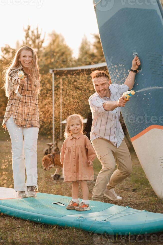 the family is resting next to their mobile home. Dad, mom and daughter play on sup boards with water pistols near the motorhome photo