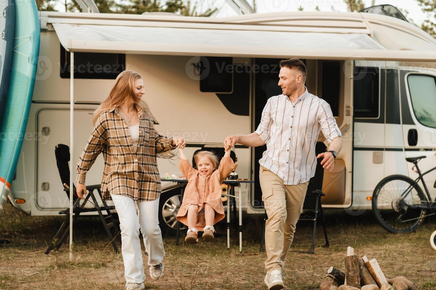 a young family is resting near their mobile home. Dad, mom and daughter play near the motorhome photo