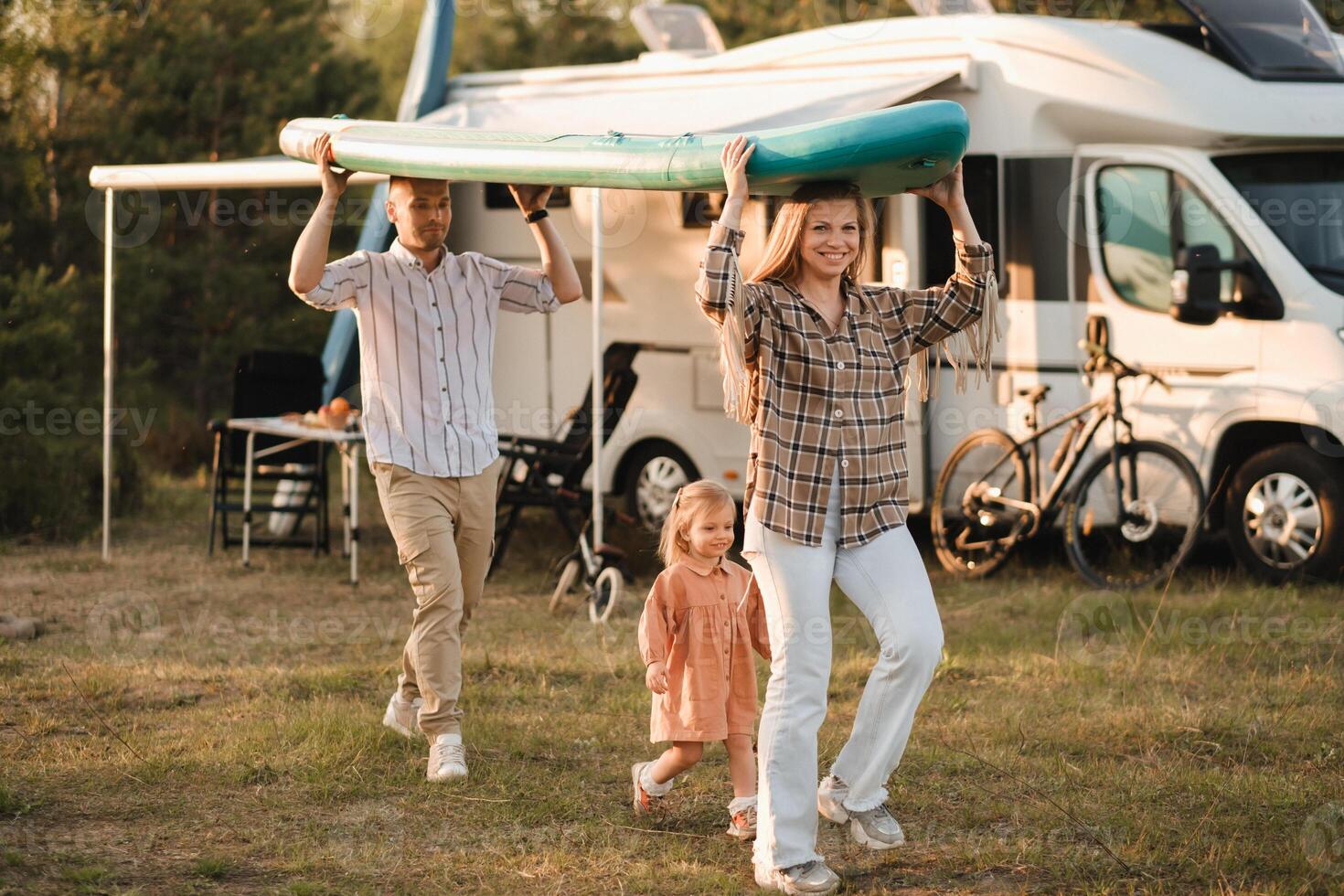 a young family is playing next to their mobile home. Dad and mom are carrying a sup board and daughter is walking next to photo