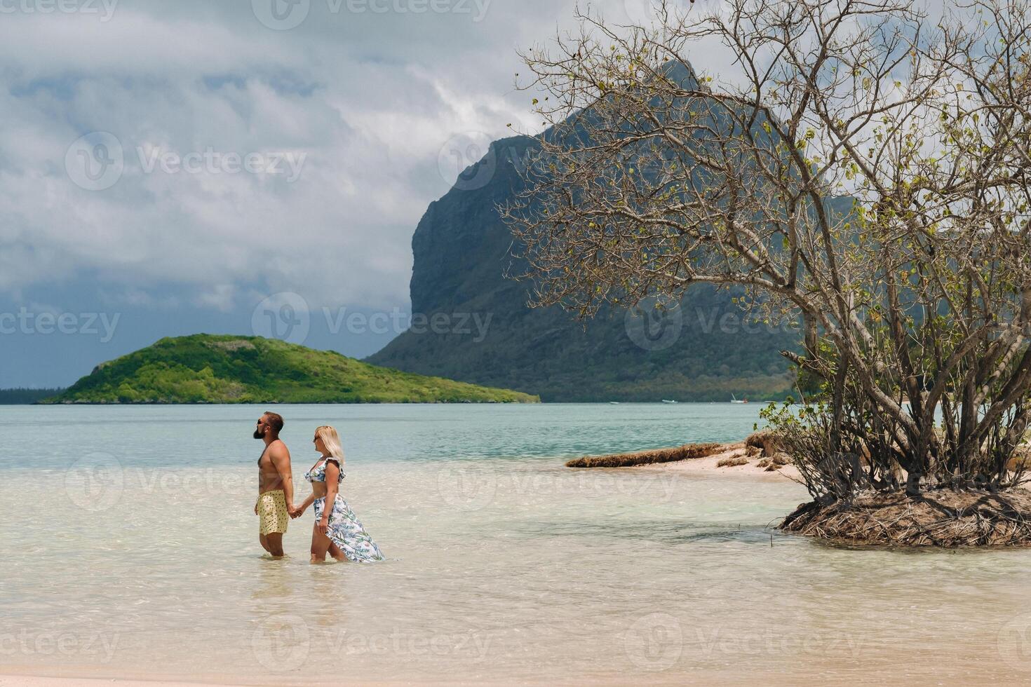 A girl in a swimsuit and a man in shorts stand in the ocean against the backdrop of mount Le Morne on the island of Mauritius.A couple in the water look into the distance of the ocean photo