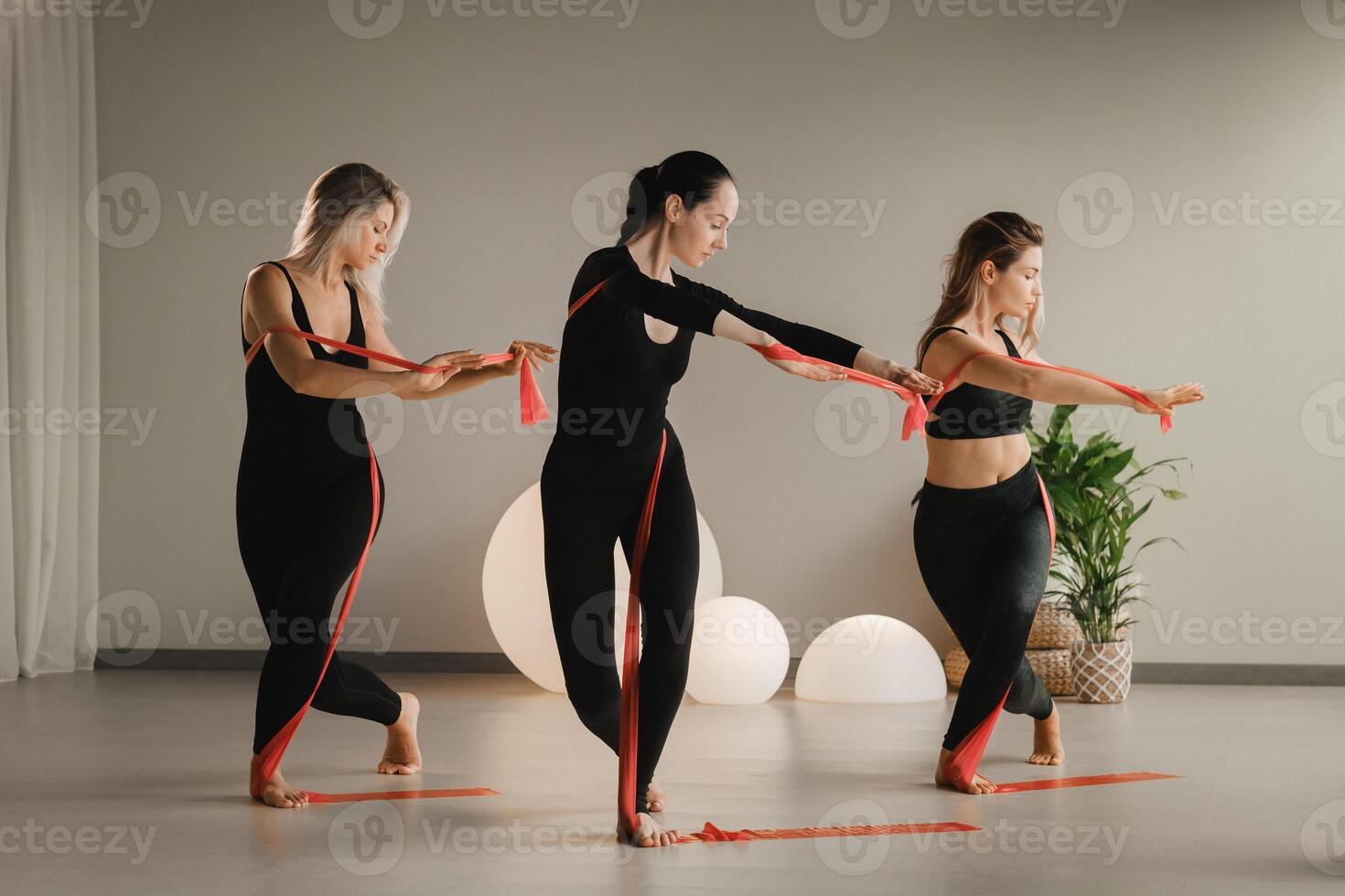 Girls in black are doing fitness with red ribbons indoors photo
