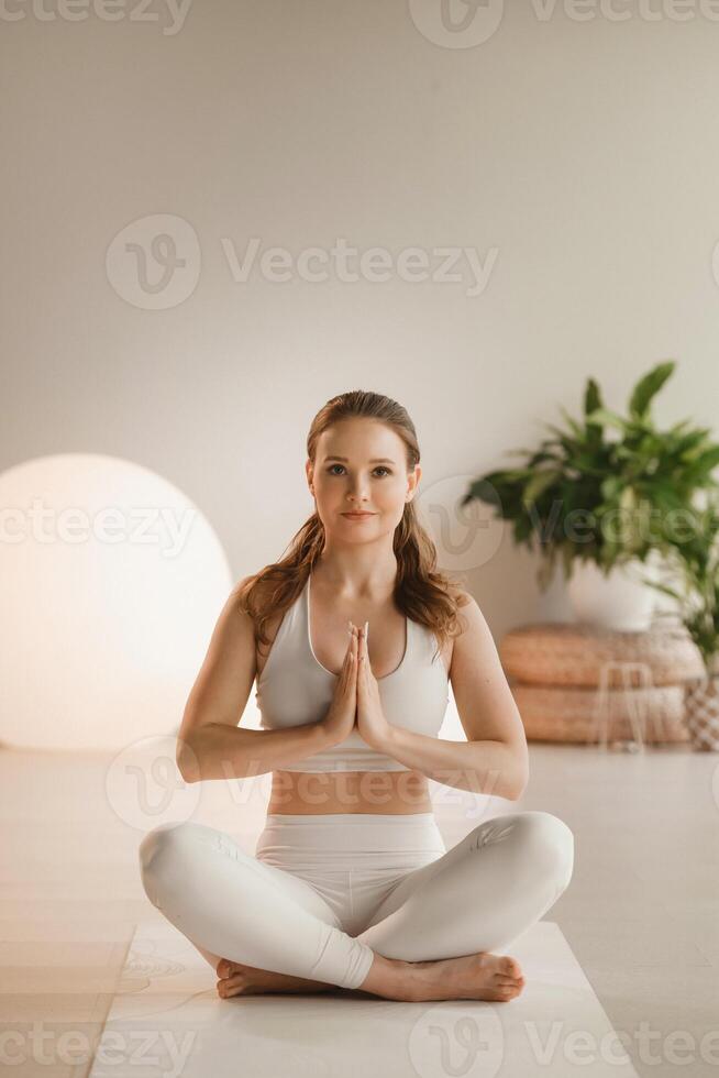 retrato de un niña en blanco ropa sentado en un loto posición en un estera a un interior yoga clase foto