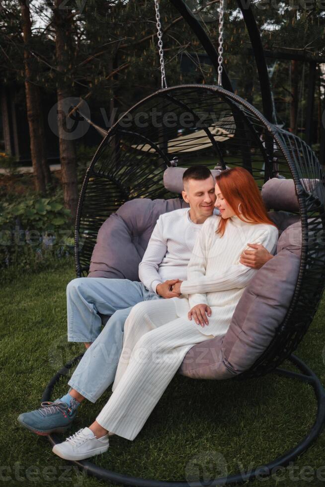 A happy family is sitting in a hammock on the lawn near the house photo