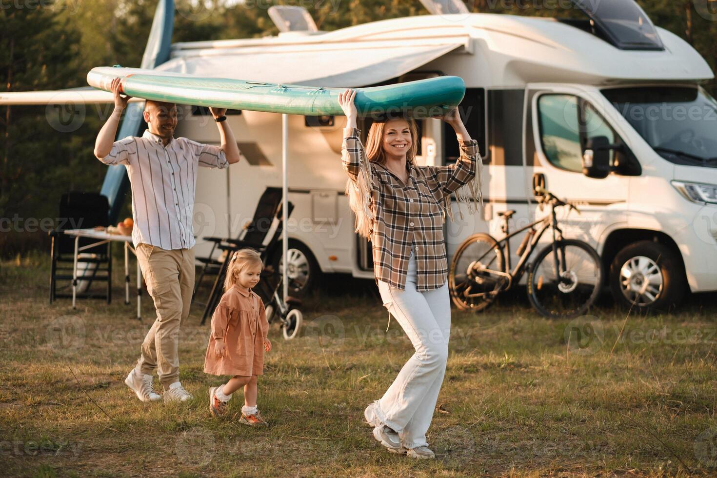 a young family is playing next to their mobile home. Dad and mom are carrying a sup board and daughter is walking next to photo