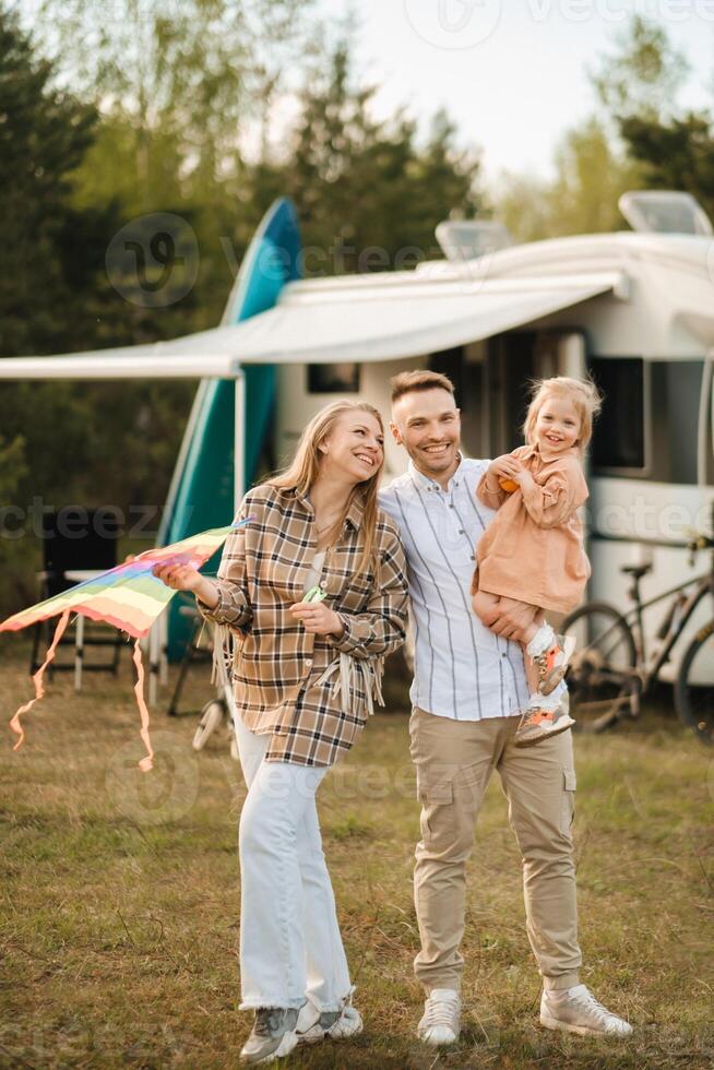 Happy parents with their child play with a kite near their motorhome in the forest photo