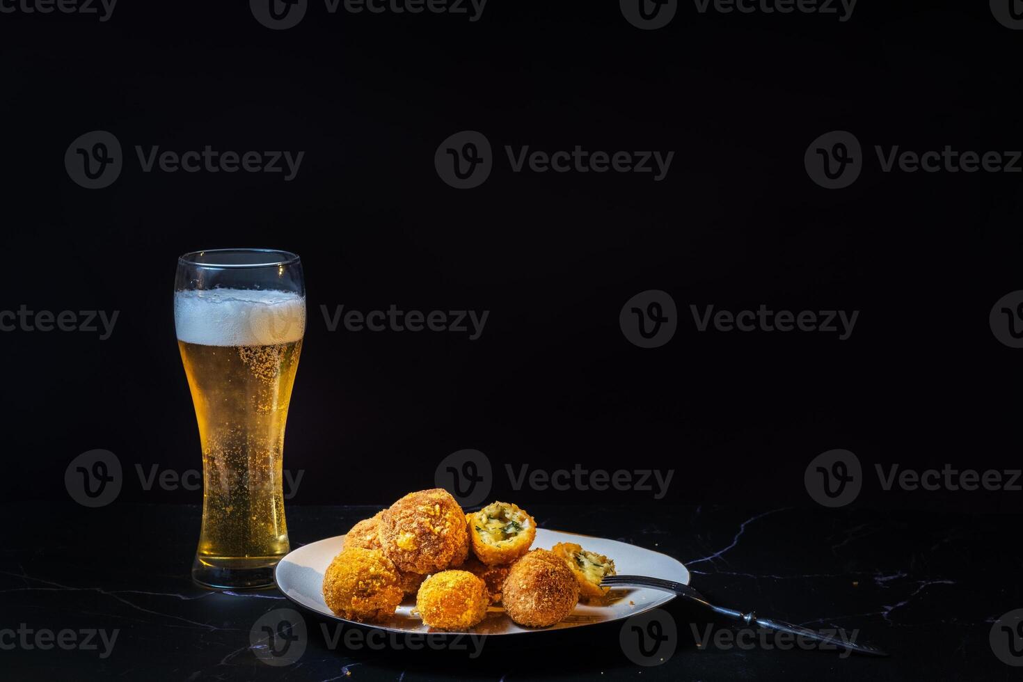 cheese balls with garlic and dill inside for a snack with a glass of beer on a black background photo