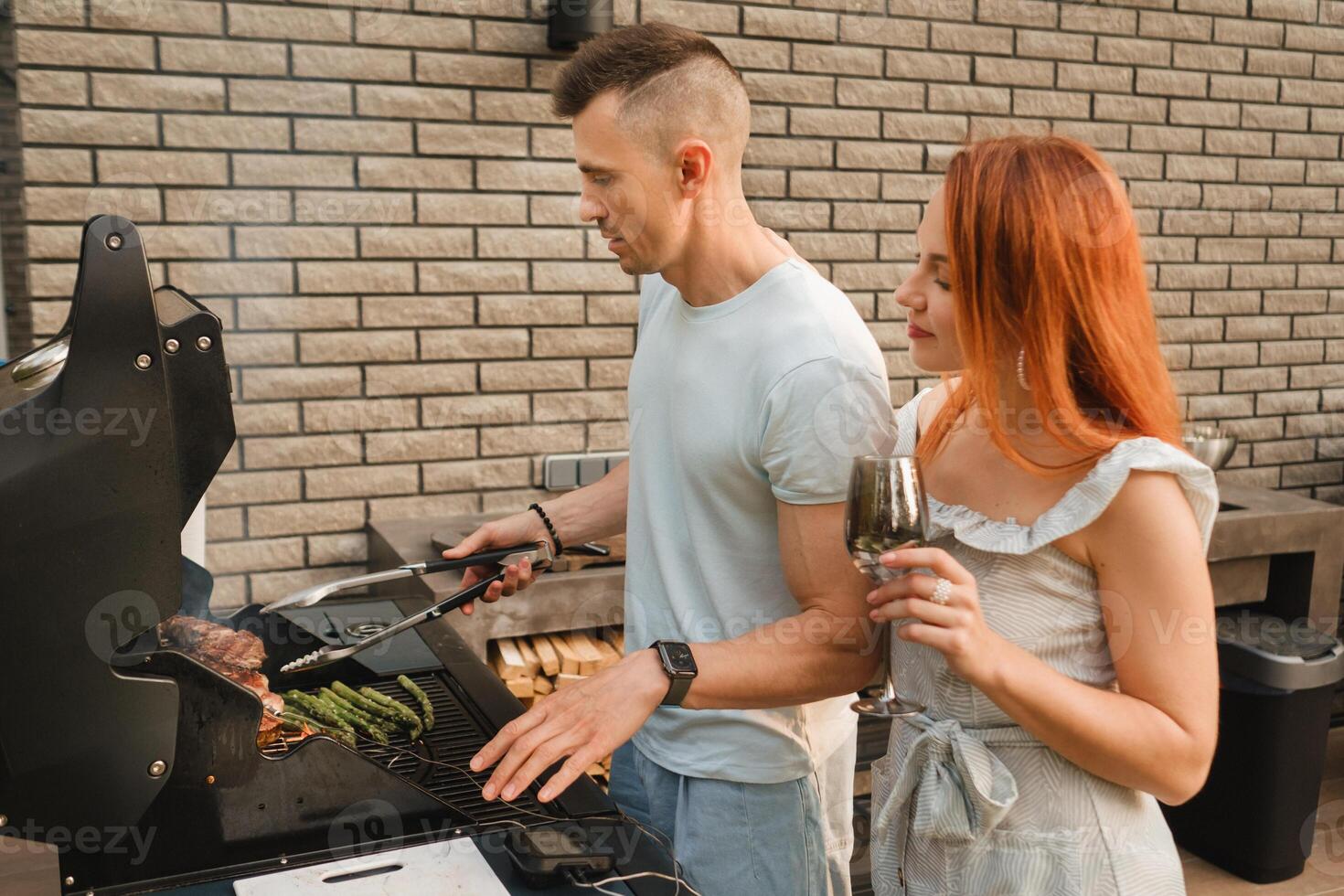 A married couple cooks grilled meat together on their terrace photo