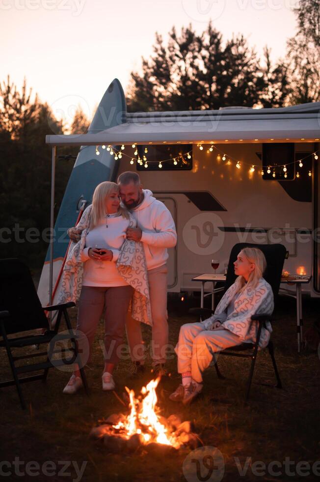 el familia es relajante juntos por el hoguera cerca su móvil hogar. noche familia vacaciones foto