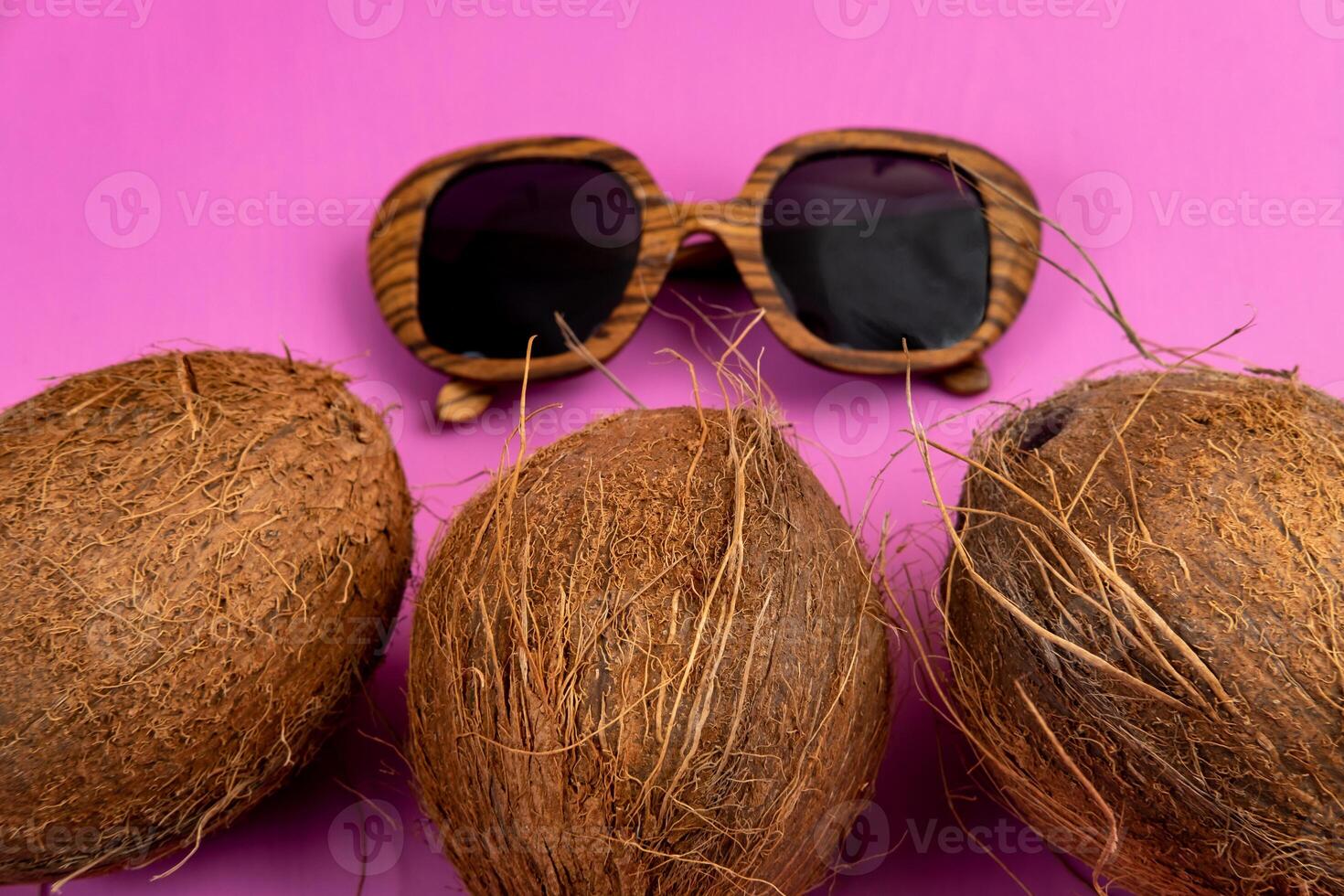three whole coconuts and wooden glasses on a pink background photo