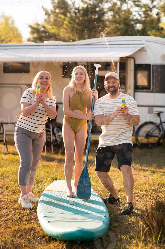 the family is resting next to their mobile home. My daughter is standing with a paddle on a sup board, and her parents pour water on her photo