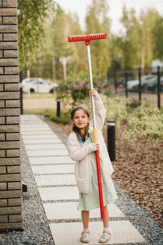 un pequeño niña con un cepillo limpia un camino en el calle en el patio foto