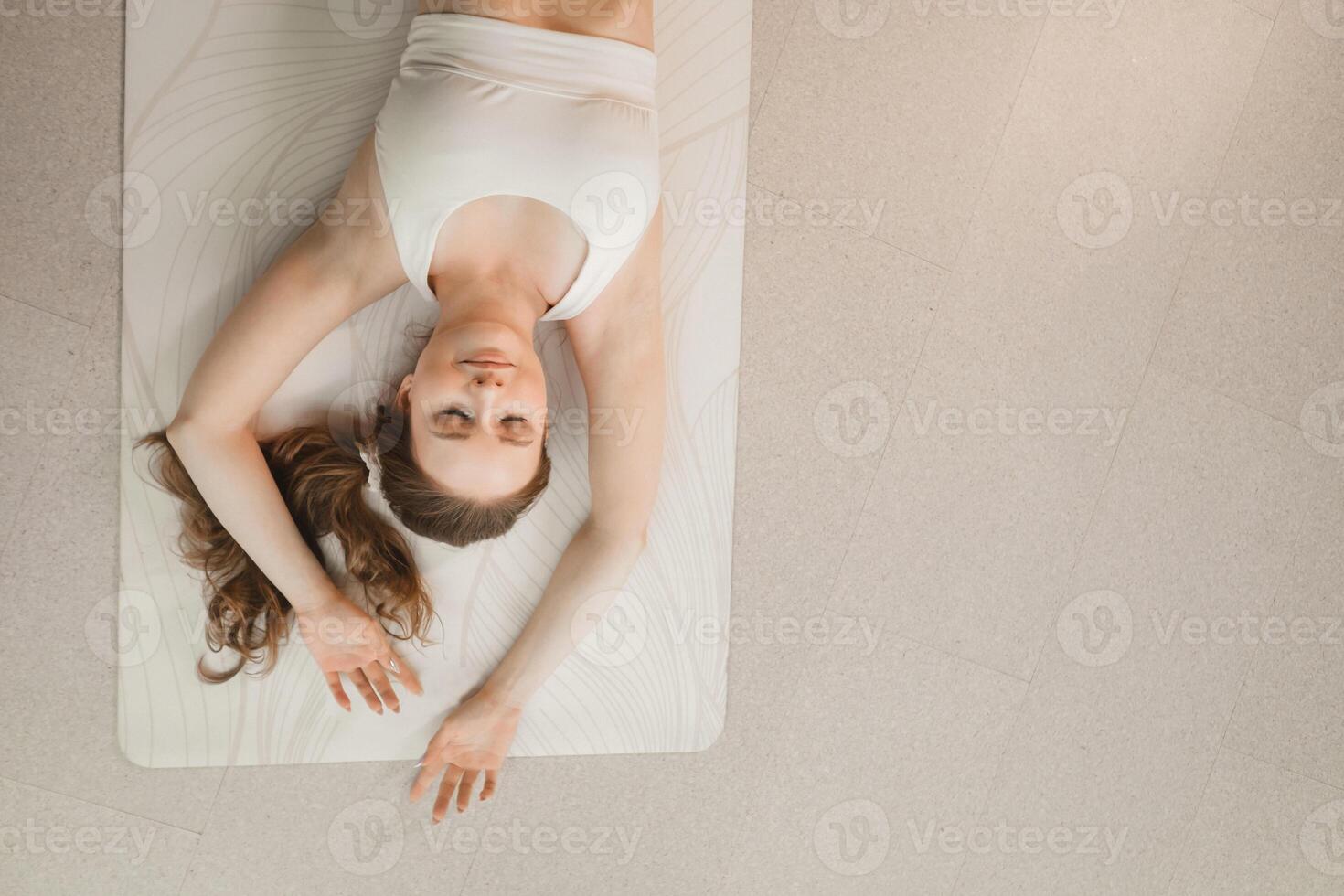 A girl in white clothes does yoga lying on a rug indoors photo