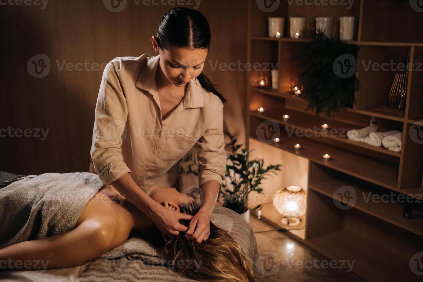 un masajista da un cabeza masaje a un mujer a el spa. un profesional masajista masajes el cabeza de un niña acostado en un spa centrar foto