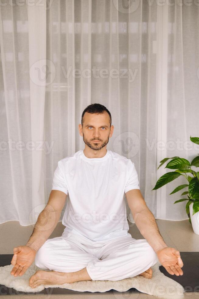 un hombre en blanco ropa de deporte es haciendo yoga con un aptitud habitación. el concepto de un sano estilo de vida foto