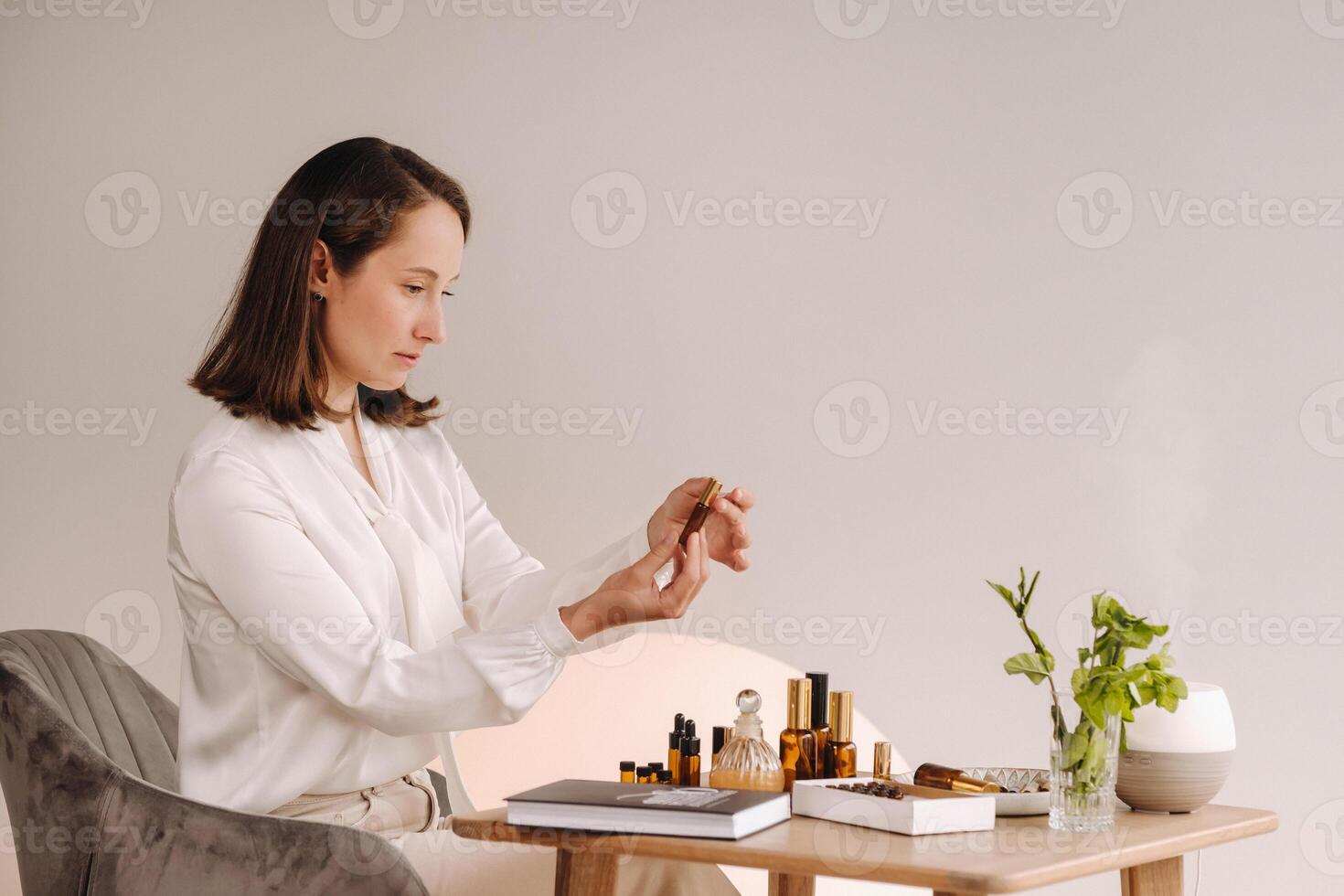 The aromatherapist girl is sitting in her office and holding a bottle of aromatic oils. there are essential oils on the table photo