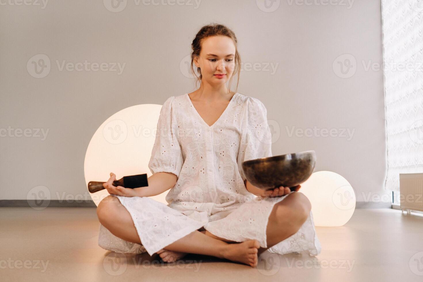 Portrait of a female yoga teacher playing a Tibetan bowl or singing a bell in the gym during a yoga retreat photo