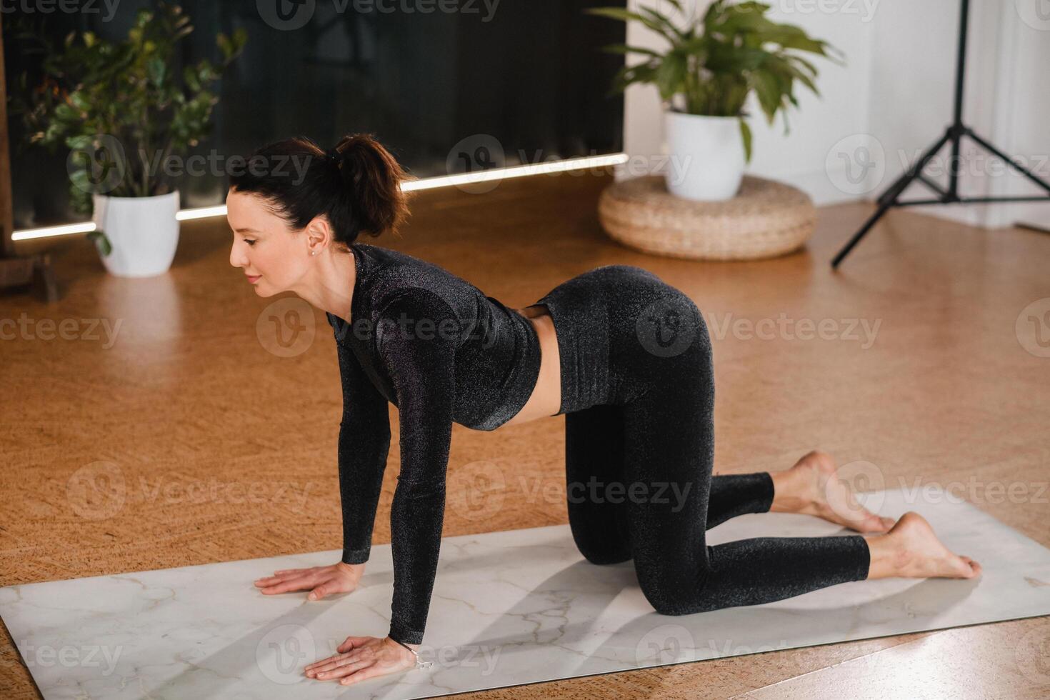 A girl in a black sports uniform does yoga standing on a mat in the gym photo