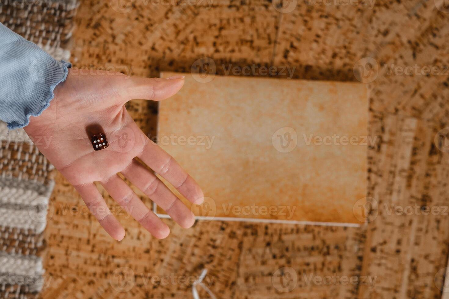 There is a dice in a person's hand. Close-up of a hand with a dice on the background of a notebook photo