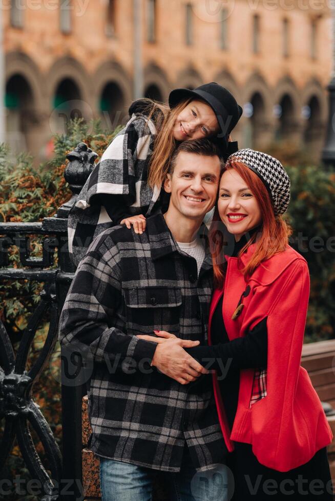 A stylish family of three strolls through the autumn city posing for a photographer . Dad, mom and daughter in the autumn city photo