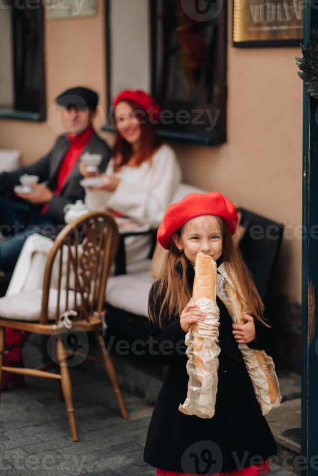 un elegante niña con baguettes soportes cerca el Tienda en contra el antecedentes de su padres foto
