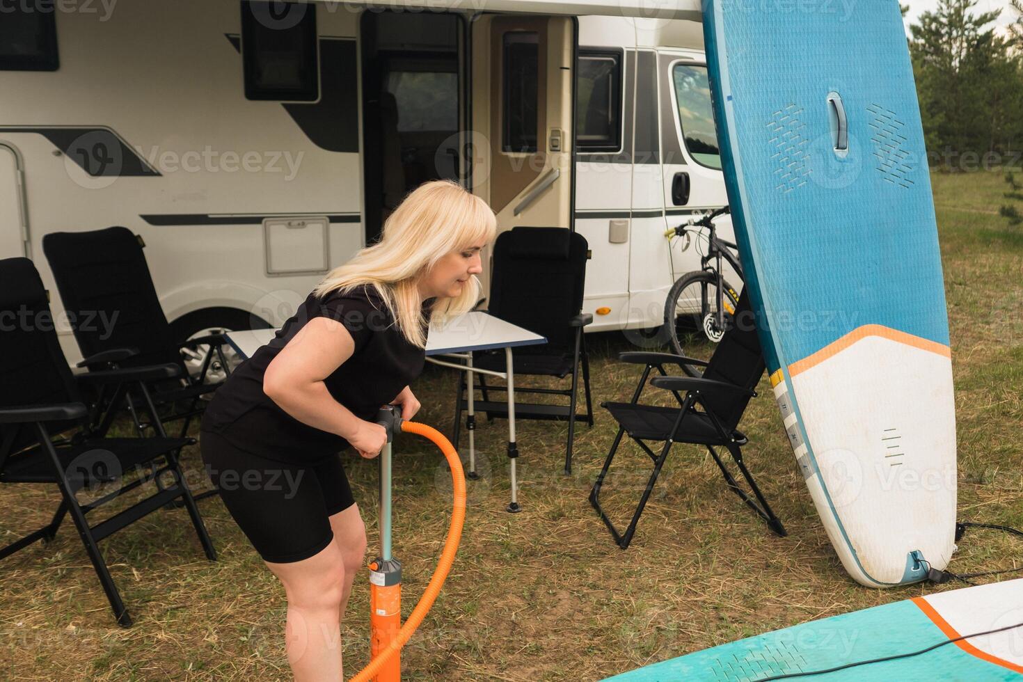 A woman inflates a sup-board for swimming near her motorhome photo
