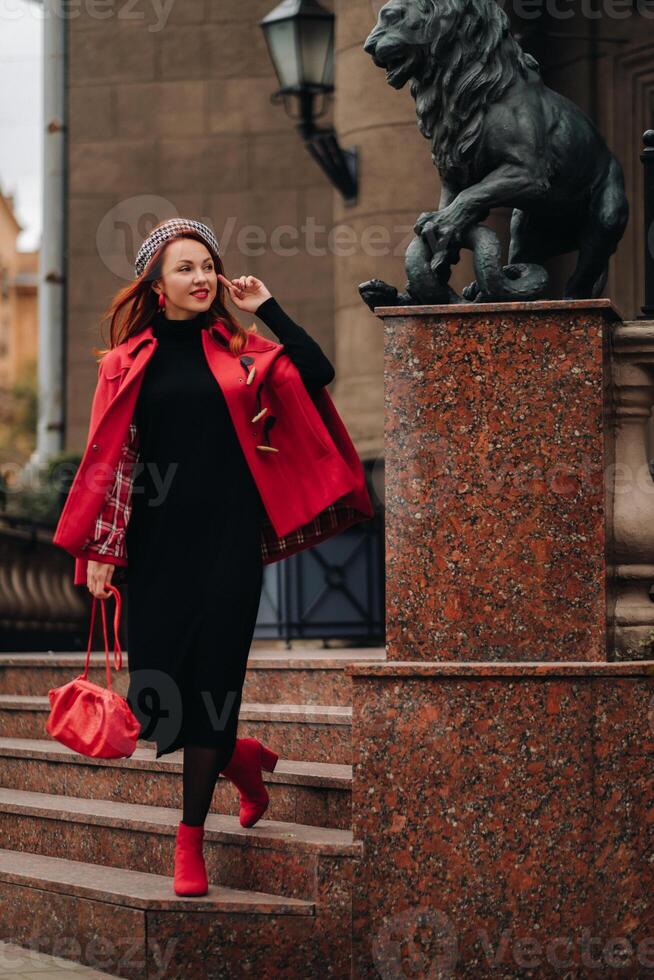 A beautiful stylish woman dressed in an elegant red coat with a stylish red handbag in the autumn city photo