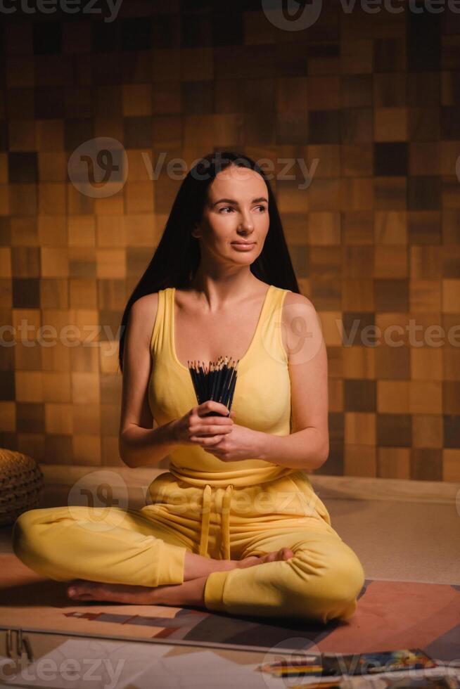 A girl in yellow clothes sitting on the floor holding pencils for drawing photo