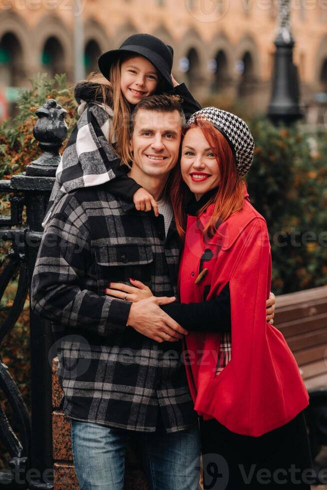 A stylish family of three strolls through the autumn city posing for a photographer . Dad, mom and daughter in the autumn city photo