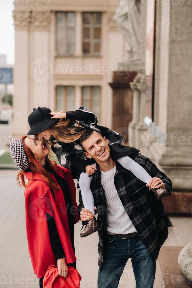 A stylish family of three strolls through the autumn city posing for a photographer . Dad, mom and daughter in the autumn city photo