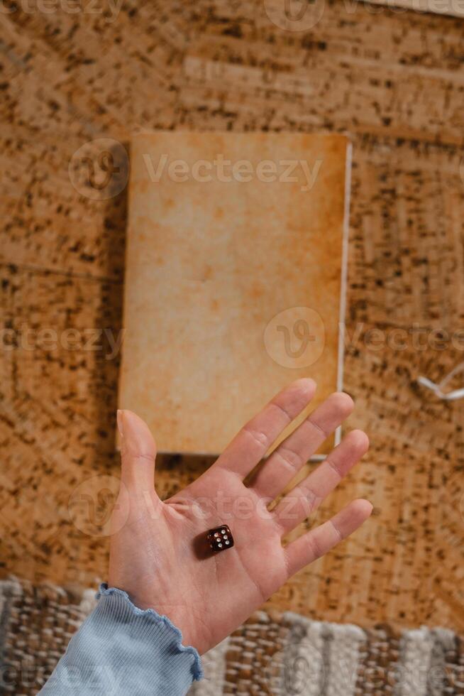 There is a dice in a person's hand. Close-up of a hand with a dice on the background of a notebook photo