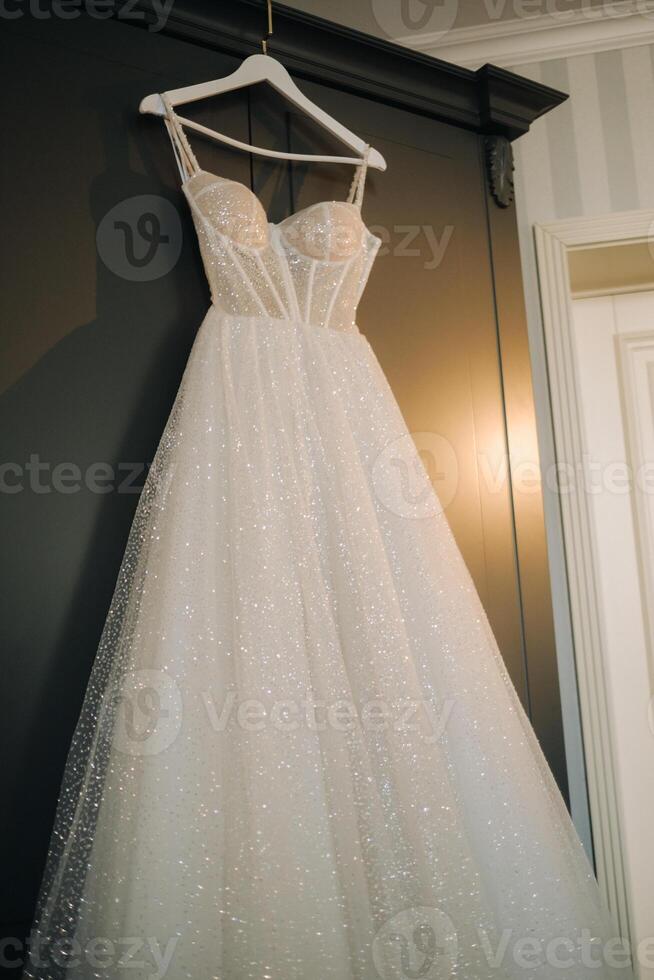 White wedding dress hanging on a hanger in a hotel room photo