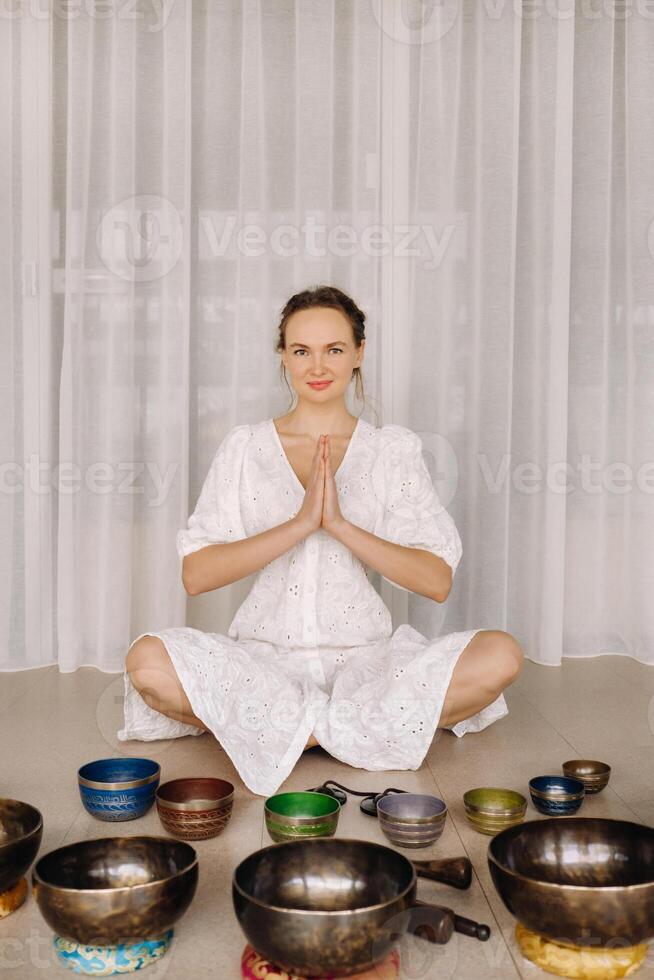 A woman sits with Tibetan bowls in the lotus position before doing yoga in the gym photo