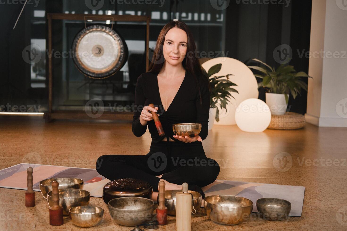 A woman in the lotus position using a singing bowl indoors . Relaxation and meditation. Sound therapy, alternative medicine. Buddhist healing practices photo