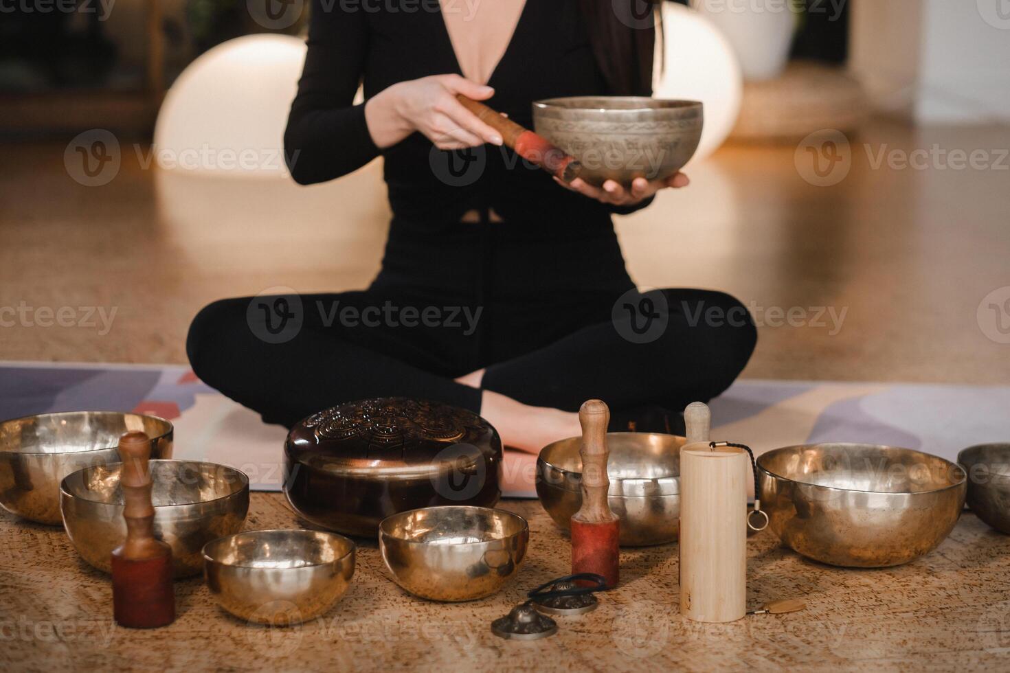 A woman in the lotus position using a singing bowl indoors . Relaxation and meditation. Sound therapy, alternative medicine. Buddhist healing practices photo