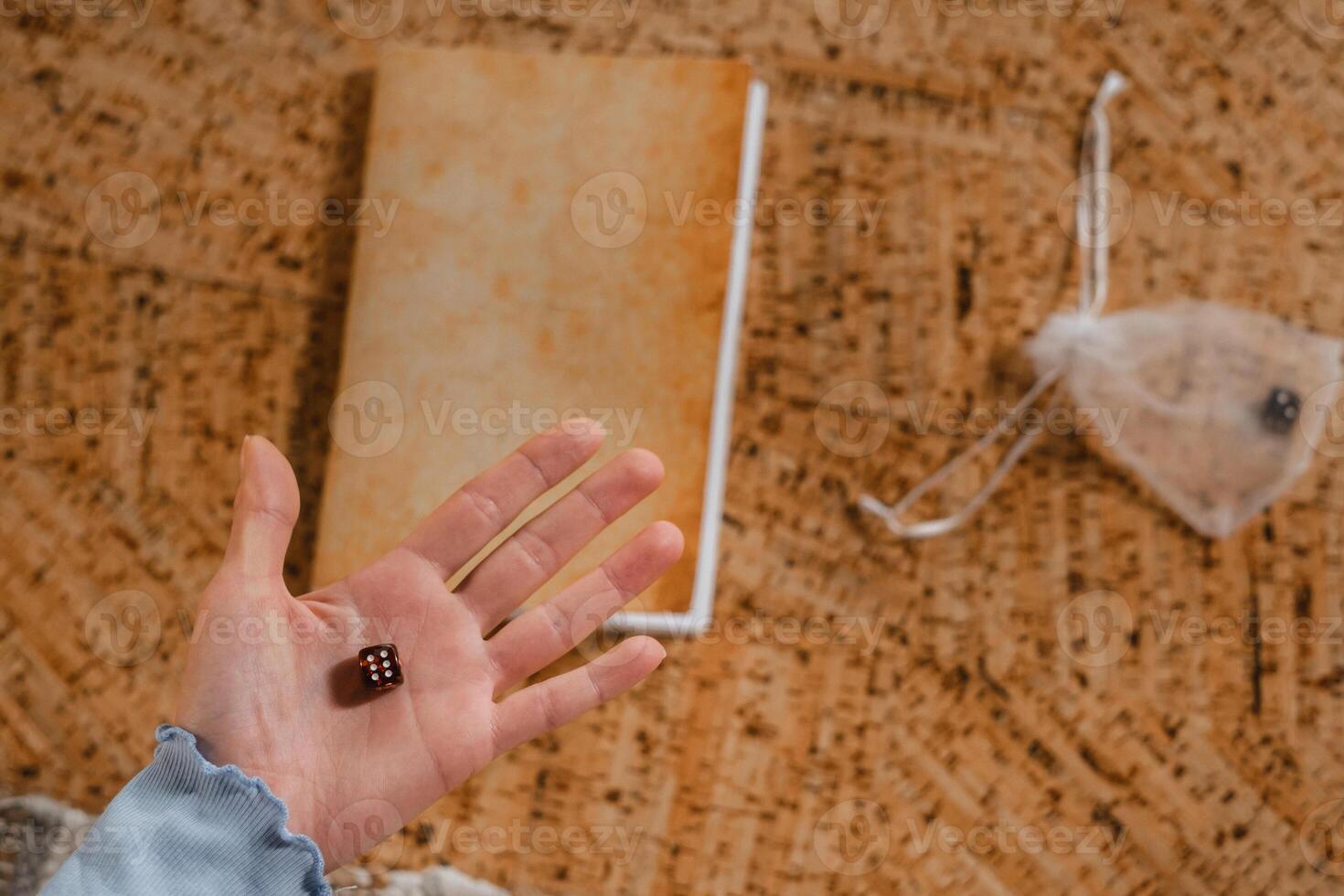 There is a dice in a person's hand. Close-up of a hand with a dice on the background of a notebook photo