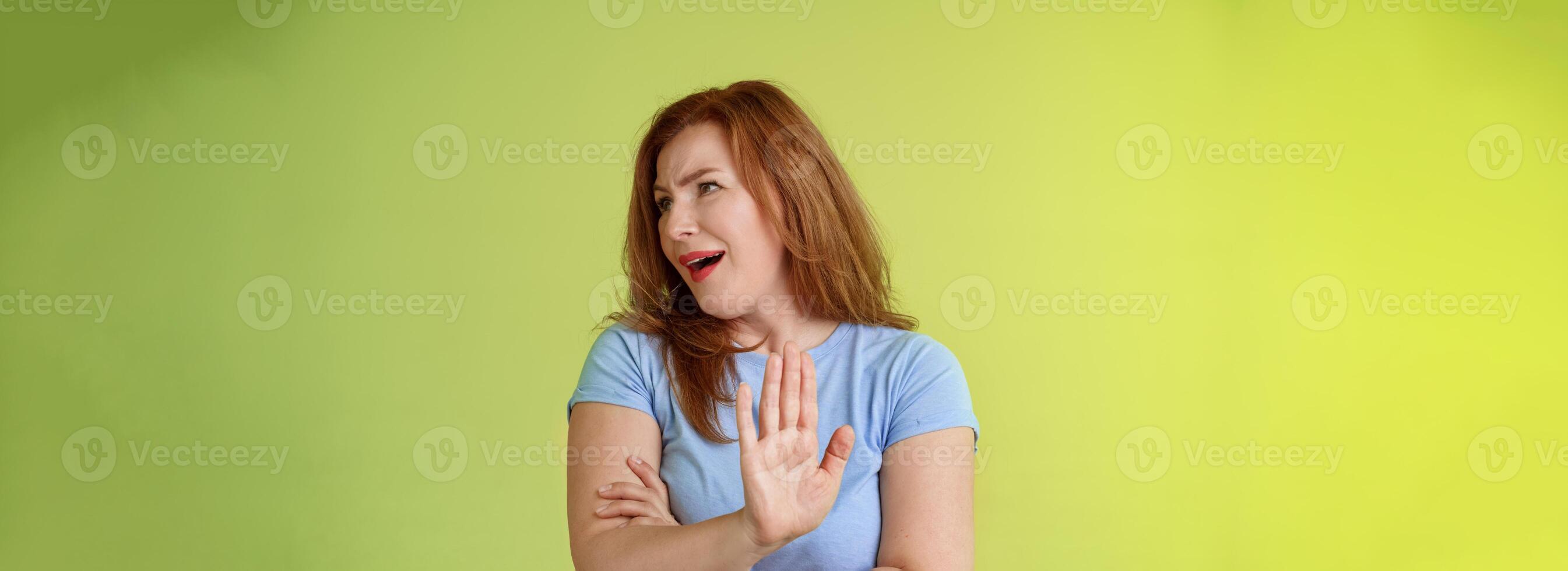 Enough wasting my time. Ignorant uninterested redhead mature woman turn away displeased reluctant show stop no gesture hold palm refusal rejecting unpleasant offer green background photo