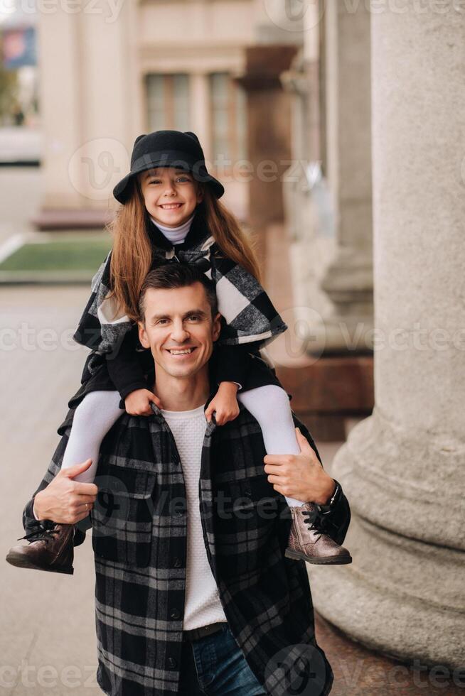 A cheerful Daughter is sitting on dad's shoulders and walking around the autumn city photo