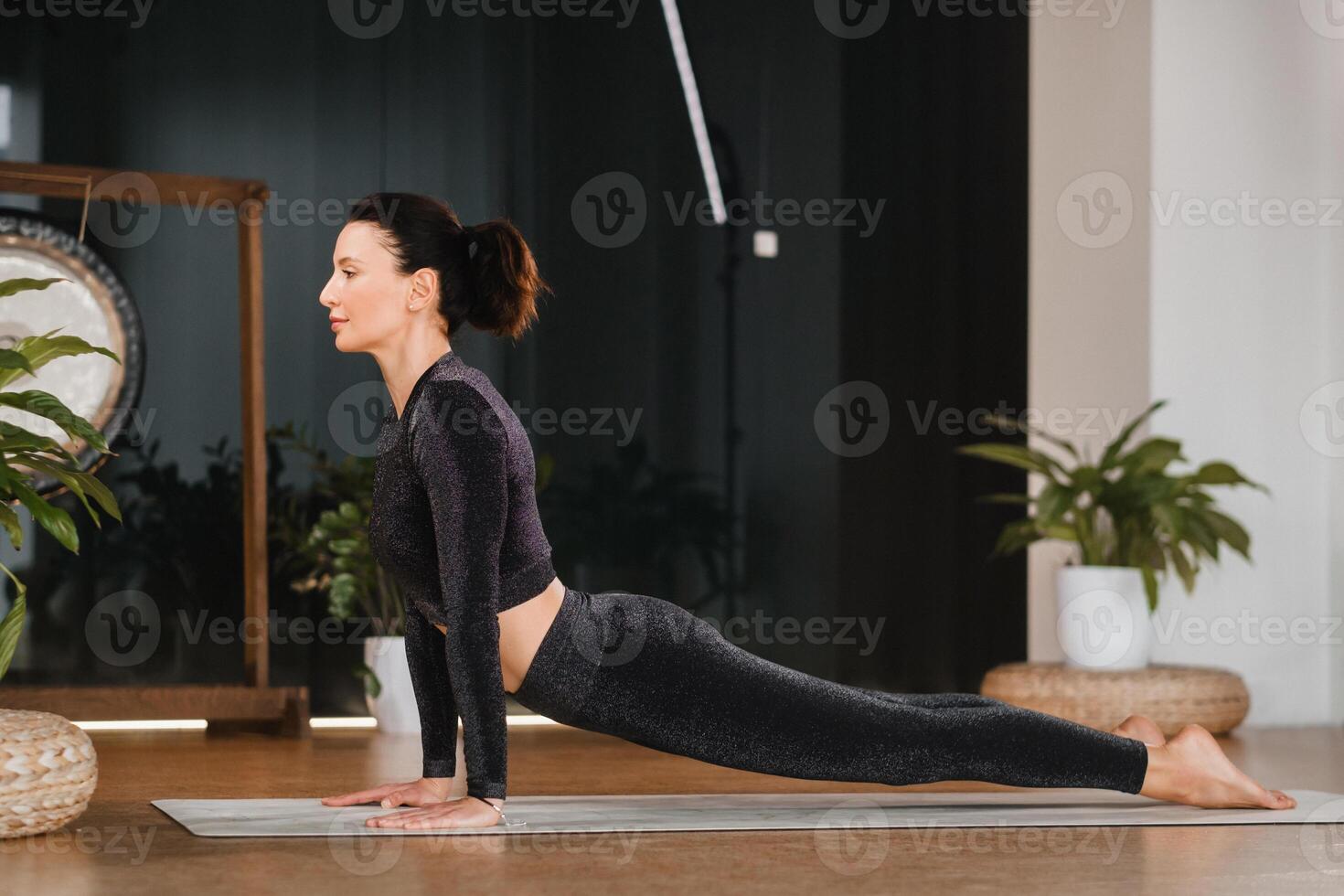 A girl in a black sports uniform does yoga standing on a mat in the gym photo