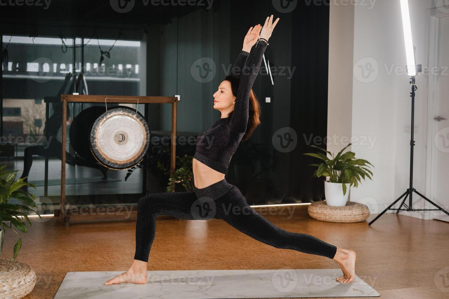 A girl in a black sports uniform does yoga standing on a mat in the gym photo
