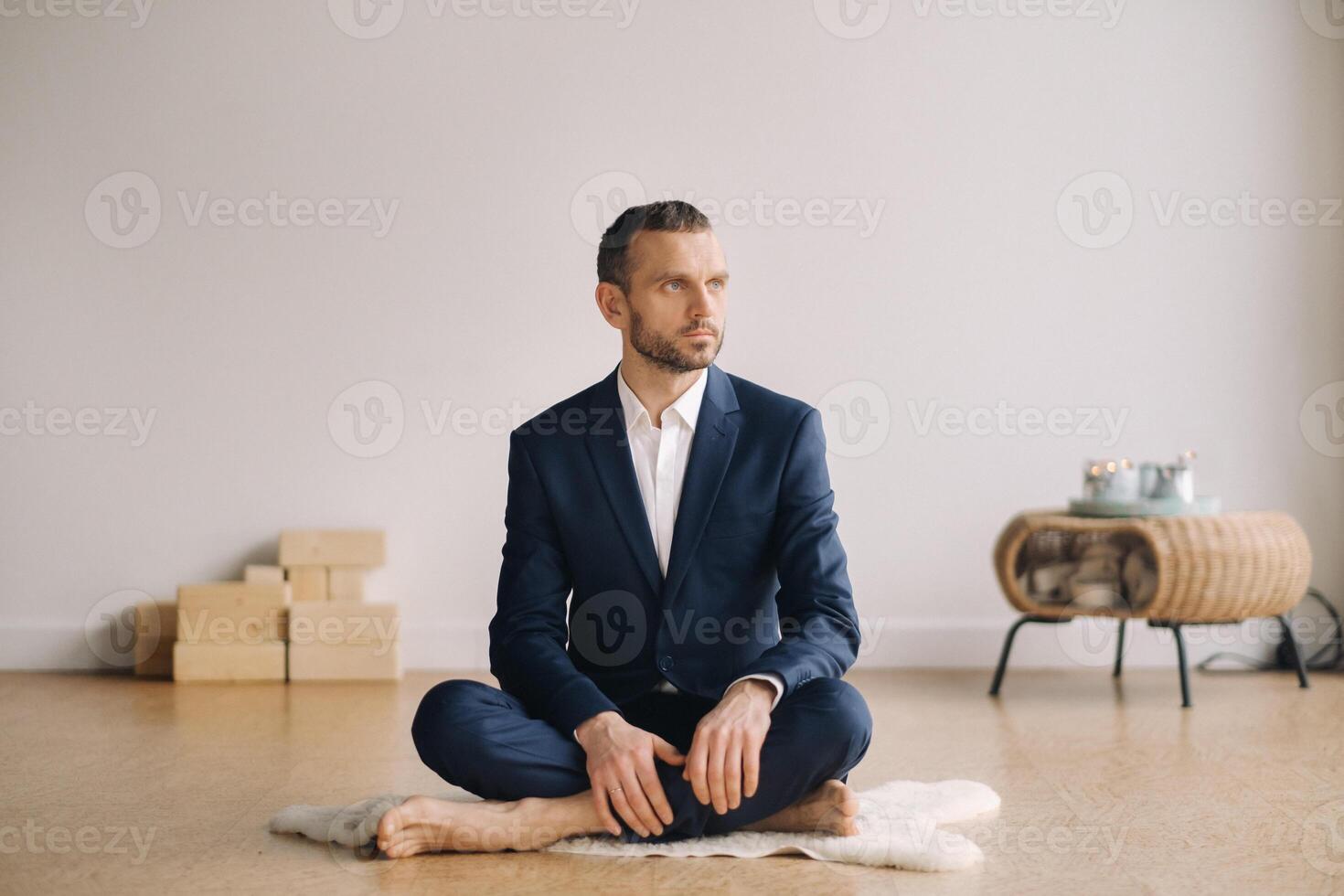 A man in a strict suit does Yoga while sitting in a fitness room photo
