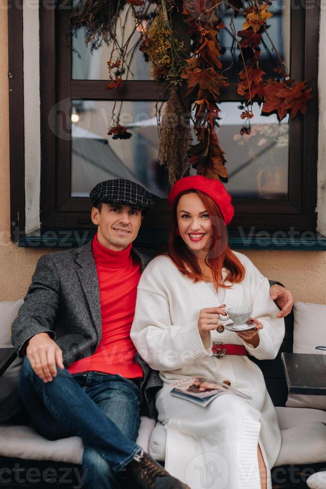 A happy stylish couple drinks coffee and smiles while sitting in a cafe on the street photo