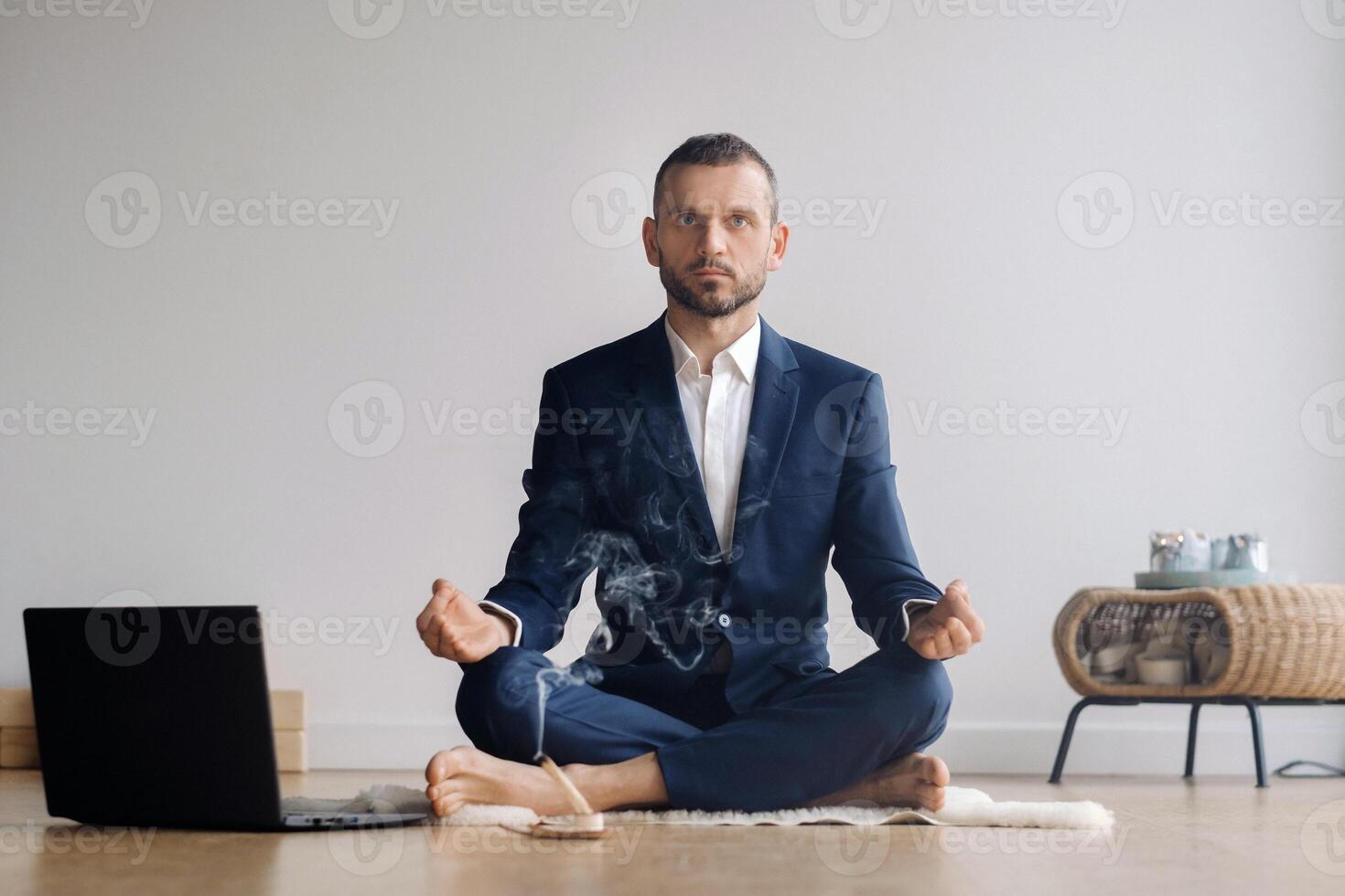 A man in a formal suit meditates while sitting in a fitness room with a laptop photo